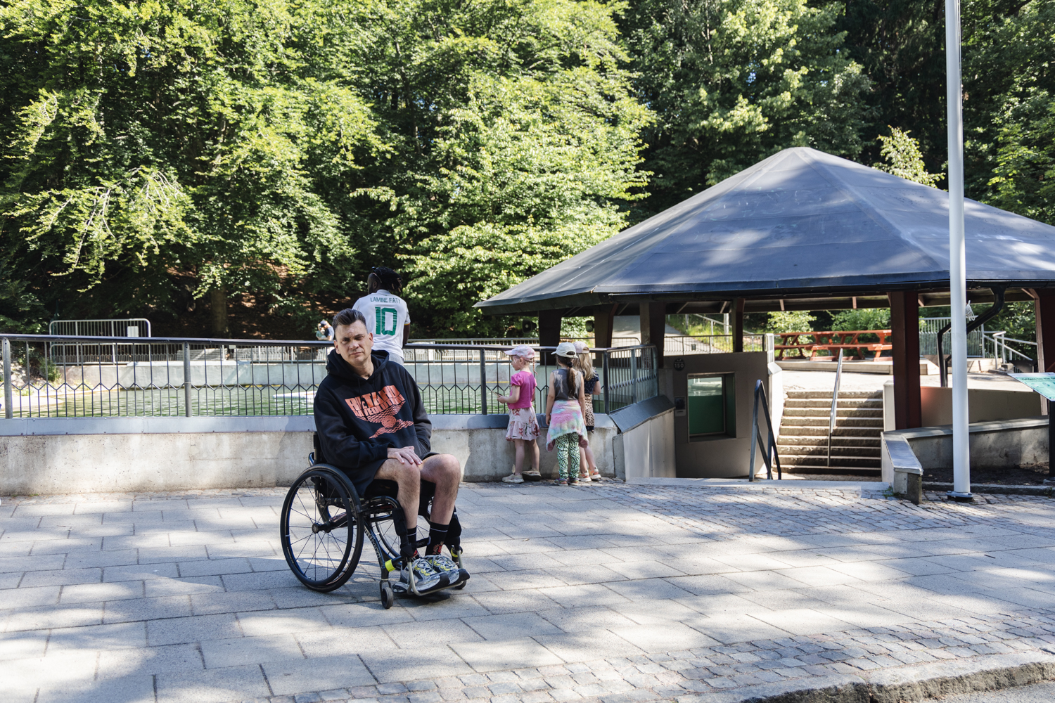 Anders Westgerd i rullstol sitter framför en säldamm, utomhus, parkmiljö.